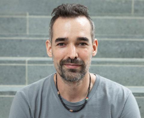 headshot of man with short hair and goatee, wearing tshirt and necklace